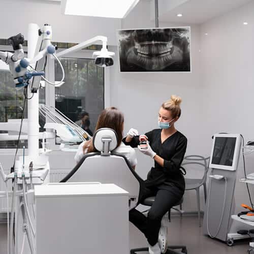 Dental Assistant educating patient about bone graphs using a model of a full set of teeth